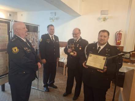 Przewodniczący Rady Miejskiej Czesław Greń oraz Naczelnik OSP Bąków Marcin Kajstura wręczają statuetkę św. Floriana i tabliczkę pamiątkową z życzeniami